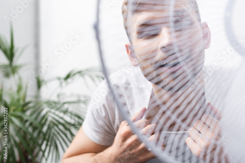 happy man feeling comfortable with electric fan at home during summer heat  selective focus