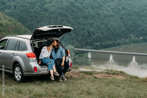 Young Stylish Traveling Hipsters Having Fun Sitting in Car Trunk Near the River Canyon, Travel and Road Trip Concept © Romvy