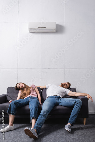 exhausted couple suffering from heat while sitting home with broken air conditioner