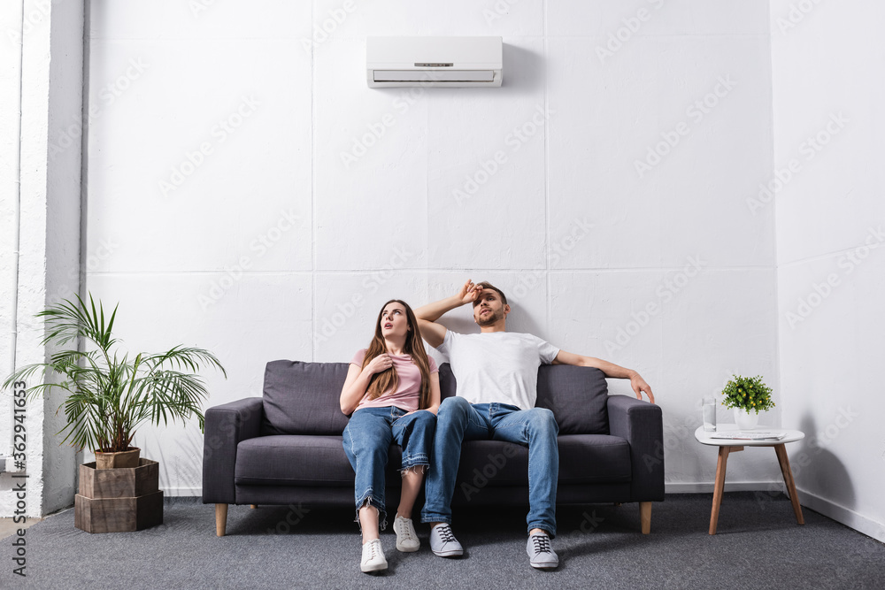 Obraz premium young sad couple suffering from heat while sitting home with broken air conditioner