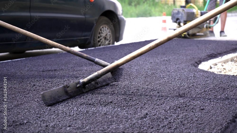 Close-up,working men shoveling black gravel for laying asphalt on the road and sidewalk,working outdoors,hard work.Laying asphalt with a manual vibratory roller. Close-up,working men shoveling black gravel for laying asphalt on the road and sidewalk,working outdoors,hard work.Laying asphalt with a manual vibratory roller.