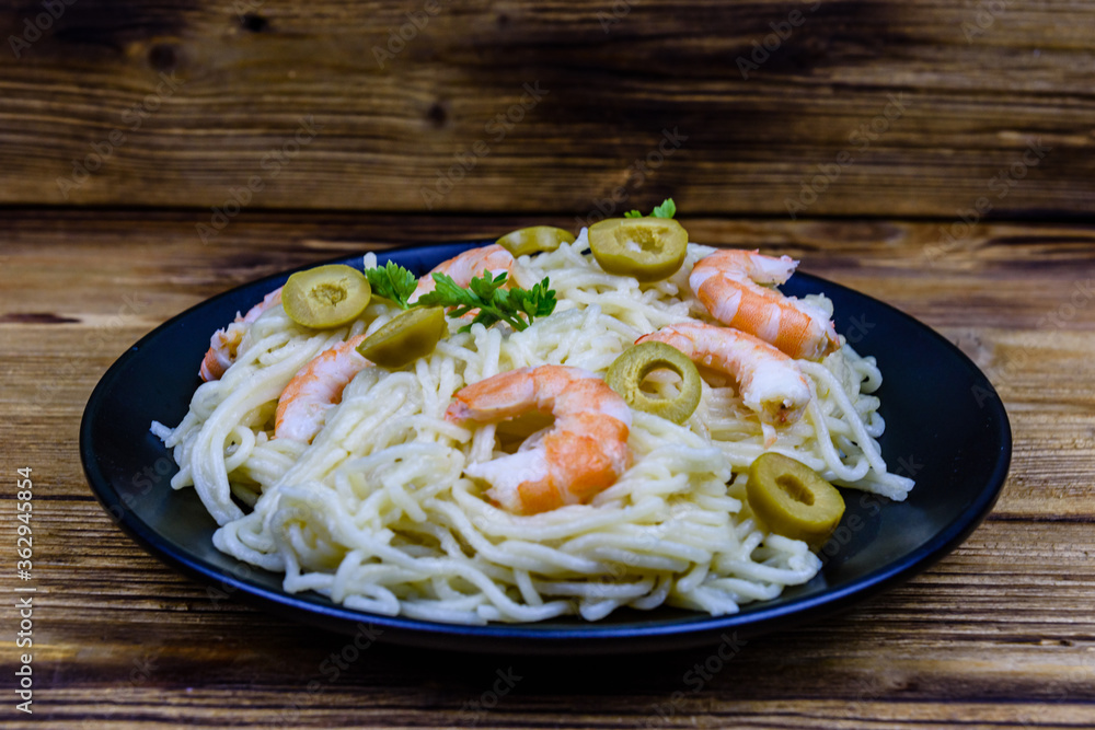 Italian pasta with shrimps and olives in a black plate Italian pasta with shrimps and olives in a black plate
