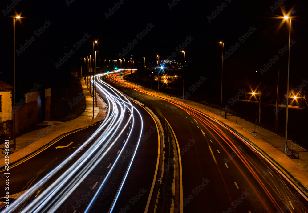 Road illuminated by trails of colored lights left by cars as they pass