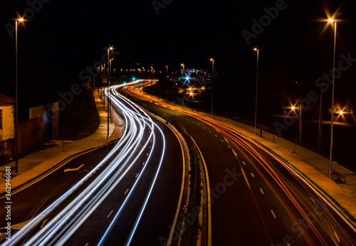 Road illuminated by trails of colored lights left by cars as they pass