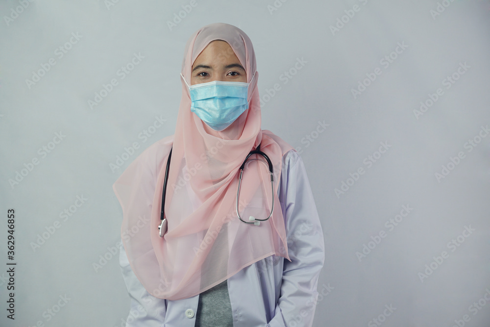 Portrait of friendly, smiling confident Muslim woman doctor in hijab dress wear mask holding a stethoscope and looking at camera on white background Portrait of friendly, smiling confident Muslim woman doctor in hijab dress wear mask holding a stethoscope and looking at camera on white background