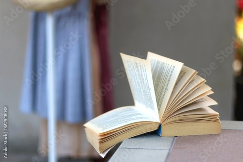 Open book in a room, clothing rack in the background. Selective focus.