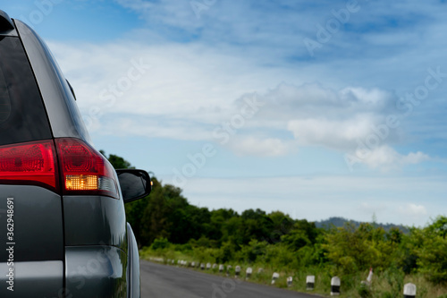 Rear of gray car with open turn light on new asphalt road. with nature of green forest and mountain under the sky.