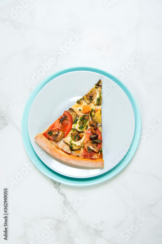 Slice of Vegan vegetable pizza. Dish with tomatoes, eggplant, champignons, Mozzarella cheese and basil pesto sauce. slice on pastel turquoise and gray serving plates. tableware on marble background 