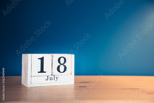 July 18 - white calendar blocks on wooden table against vintage blue background