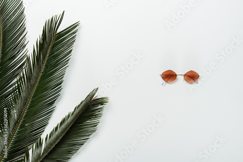 top view of green palm leaves and fashionable sunglasses on white background