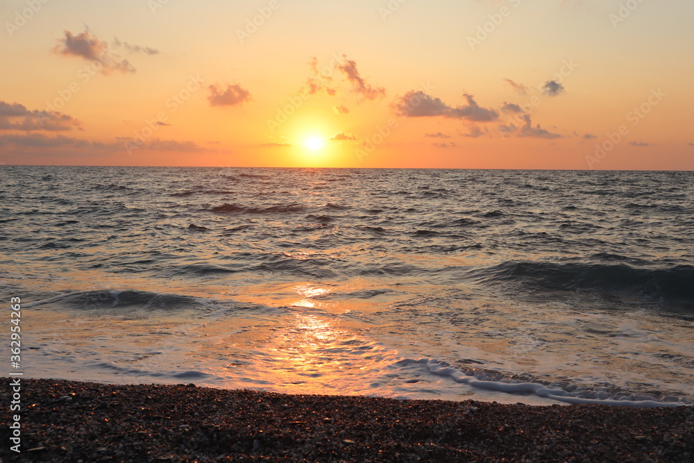 Beautiful sunset on the sea coast, reflections of the setting sun on pebbles, on sea foam and on the surface of the water, pink-orange sky, the sun and a sunny path on the surface of the sea, beach va