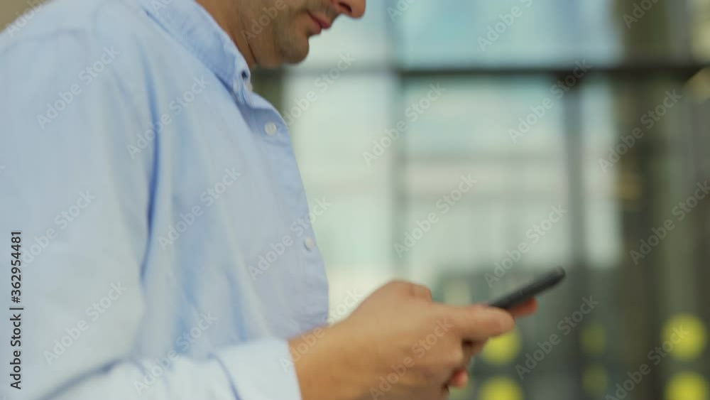 Tilt up side view tracking shot of young man in casual clothes text messaging on cell phone while walking down city street, then stopping, looking away and smiling Tilt up side view tracking shot of young man in casual clothes text messaging on cell phone while walking down city street, then stopping, looking away and smiling