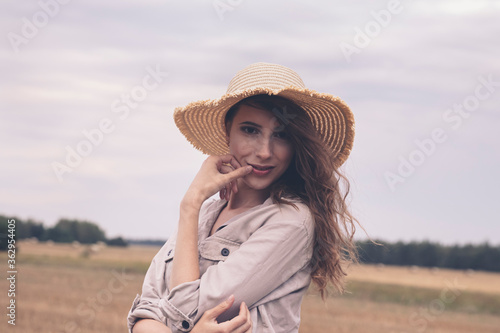 A young attractive girl in a straw hat stands in a field.