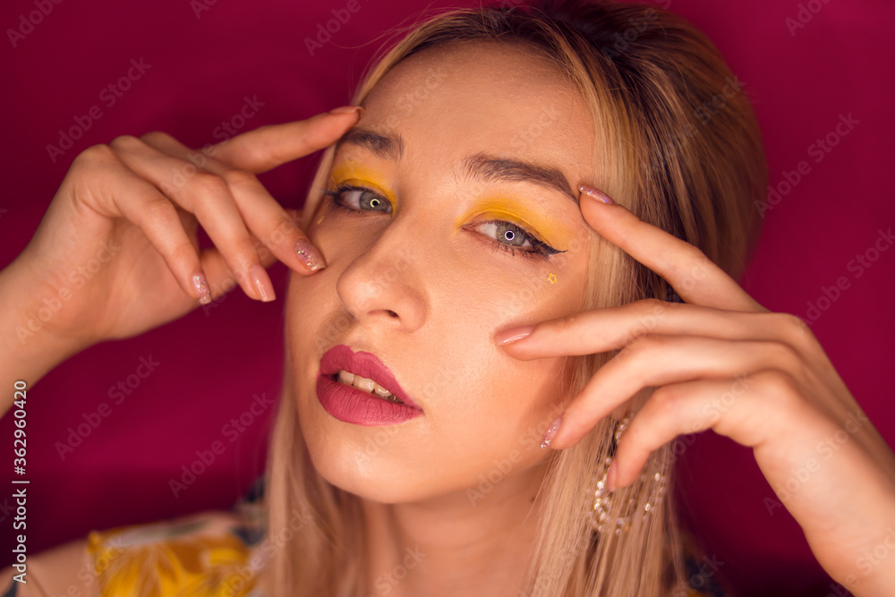 Obraz premium Girl with blond hair and yellow make-up on a pink background 