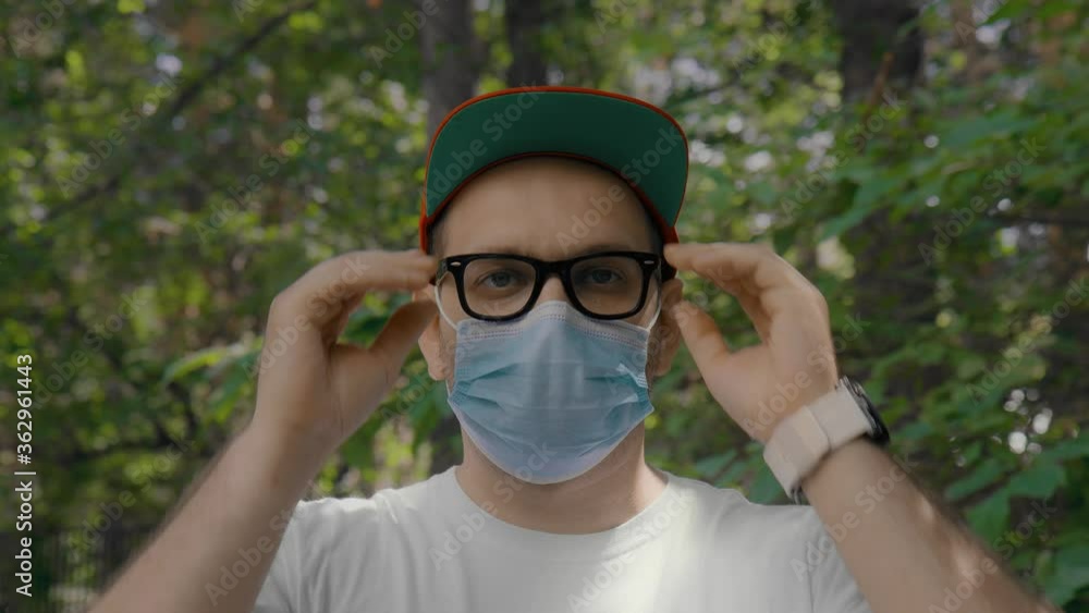 Close up: Portrait of a European guy in a medical mask protecting his face from the covid19 coronavirus. A young man in glasses and a sterile mask on the street during the pandemic. Slow motion, 4K Close up: Portrait of a European guy in a medical mask protecting his face from the covid19 coronavirus. A young man in glasses and a sterile mask on the street during the pandemic. Slow motion, 4K