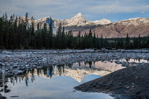 Snow capped peaks reflected in the Athabasca River in the Canadian Rockies, viewed from the Icefields Parkway, which extends from Banff to Jasper, Alberta, Canada.