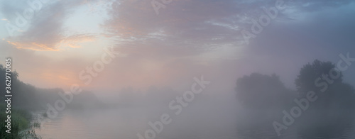 Tranquil morning landscape panorama at sunrise. Heavy fog over the river. Dawn illuminates and makes the clouds colorful. © Uladzimir