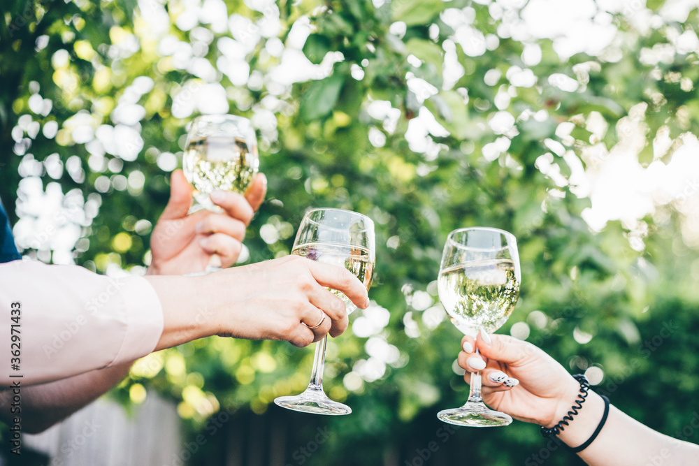 Hand holding a glass of white wine on the blurred background of green park. People holding glasses of white wine making a toast.