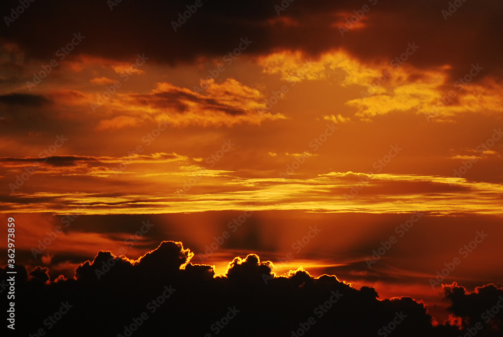 Sun emerging behind clouds powerful skyline of sunrise or sunset with golden sun rays looking cinematic like fire