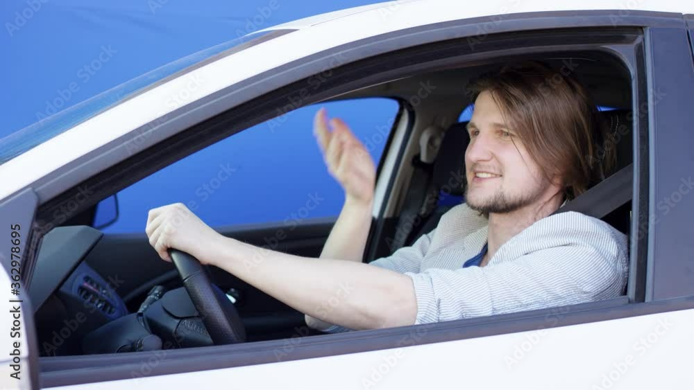 Annoyed driver in casual clothes is stuck in traffic jam. Young man is honking the horn and telling other drivers to keep driving. Brunette guy is sitting in his white car with blue background. Annoyed driver in casual clothes is stuck in traffic jam. Young man is honking the horn and telling other drivers to keep driving. Brunette guy is sitting in his white car with blue background.