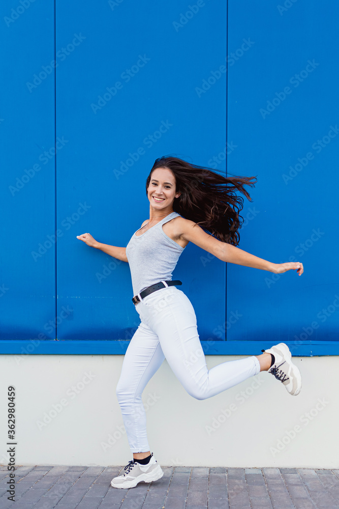 Portrait of a beautiful young woman smiling and jumping with blue background