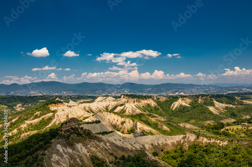 Civita di Bagnoregio, Viterbo, Tuscia, Lazio, Italy. A view of the valley of the badlands, formed by landslides and by the erosion of the tufa, lava and clayey rock. Blue sky and green mountains.