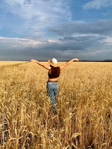 Young happy beautiful slender girl with long black hair and a hat in a wheat field. Summer landscape