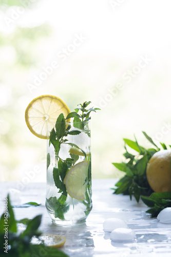 A glass with lemonade or mojito cocktail with lemon and mint, cold refreshing drink or beverage with ice on white background. Selective focus