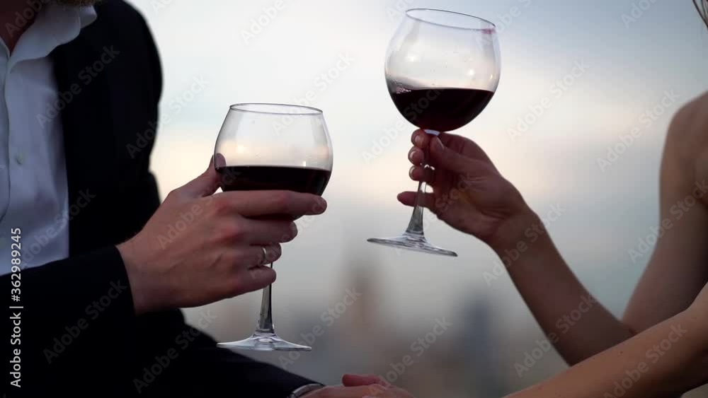 A couple in love: a man in a jacket and shirt and a girl, they sit on the roof against the background of the city. They drink wine from glasses, take each other's hands and kiss. A couple in love: a man in a jacket and shirt and a girl, they sit on the roof against the background of the city. They drink wine from glasses, take each other's hands and kiss.
