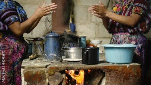 A pair of indigenous women dressed in traditional clothes make tortillas over a firewood kitchen in Guatemala.