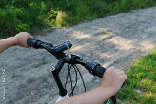 close up image of boy's hands hold black handlebar of bike while riding bicycle on countryside road. Happy summer vacation concept.