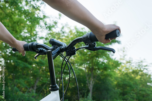 child's hands hold black handlebar of bike while riding bicycle on countryside road in green forest. Happy summer vacation concept.