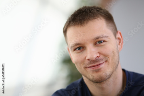 Smiling cheerful guy in black t-shirt staying in room while posing at camera. Lifestyle concept