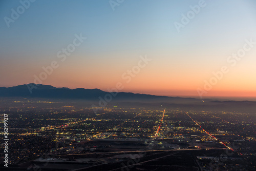 The city lights of the skyline of the Inland Empire near Los Angeles California begin to appear as the sun sets in a dramatic orange sunset. View from Potato Mountain in Claremont Wilderness Park