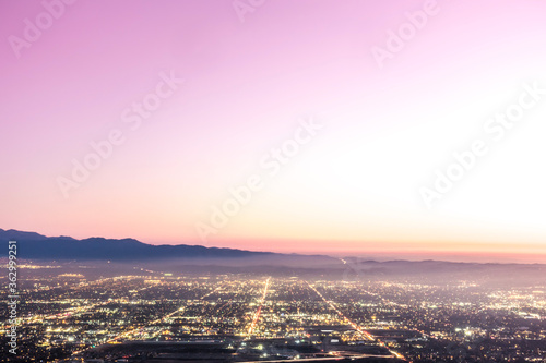 The city lights of the skyline of the Inland Empire near Los Angeles California begin to appear as the sun sets in a dramatic pink sunset. View from Potato Mountain in Claremont Wilderness Park