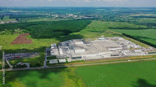 Modern factory surrounded by nature. Large area of industrial complex among green fields. Manufacturing in natural environment. Aerial view.