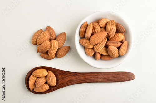 almonds in wooden spoon with almond bowl isolated on white background