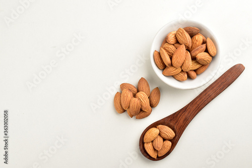 almonds in wooden spoon and white bowl isolated on white background