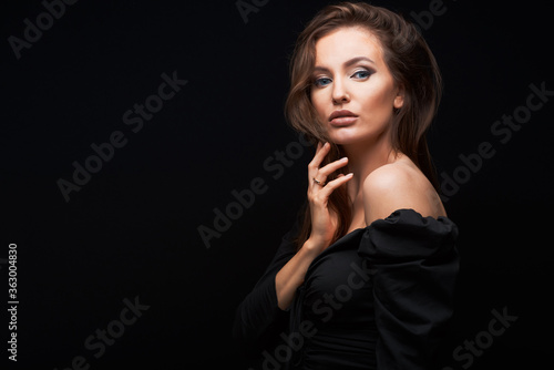 Fashion photo of a sexy caucasian woman with brown hair and bright makeup posing at studio