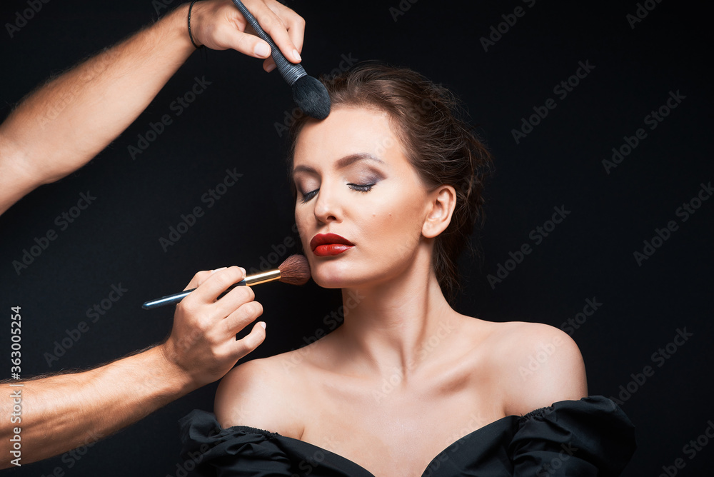 Obraz premium beautiful woman with beautiful brown hair in a dark dress on a dark background closed eyes and stylist does makeup