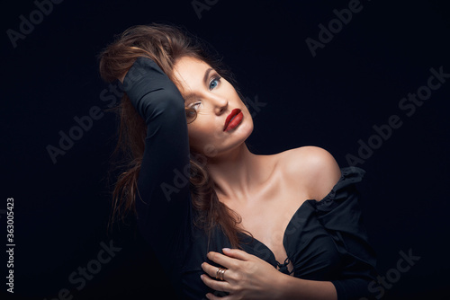beautiful fashion portrait of a lovely woman in a dark dress on a black background holding brown hair with hand