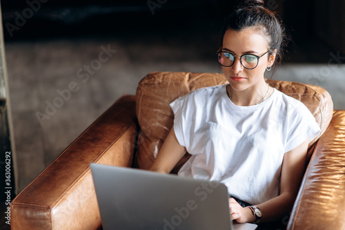 Online learning. Video call. Young cheerful girl with glasses learns distantly via video conference using a laptop while sitting at home