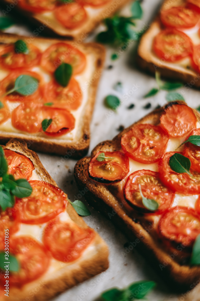 Baked sandwich with cheese and cherry tomatoes on dark bread decorated with fresh basil leaves.