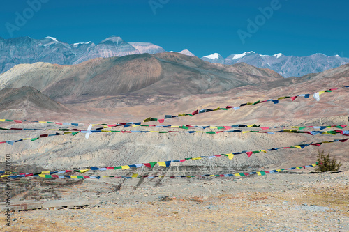 View of mountains near muktinath temple at mustang, Nepal with snow on summit. Blue sky sunny day. Colorful prayer flags at the bottom photo