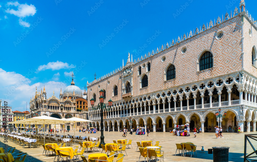 Fototapeta premium Venice, Italy - june 29th 2020 - very little tourists crossing the San Marco square and passing the empty terraces with the Saint Mark's Basilica and the Doge's Palace on a sunny Corona day in summer