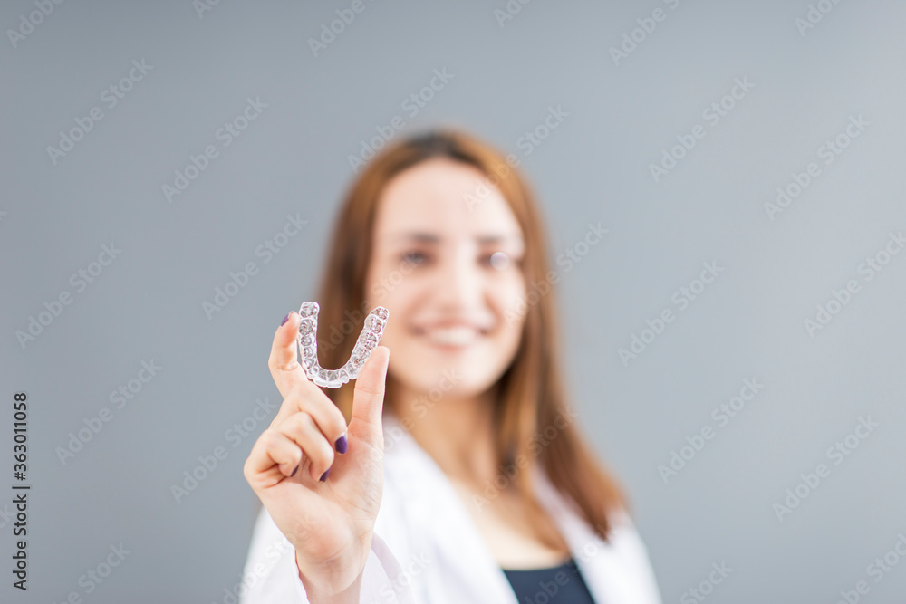 Beautiful smiling Turkish woman is holding an invisalign bracer in a studio with grey background Beautiful smiling Turkish woman is holding an invisalign bracer in a studio with grey background