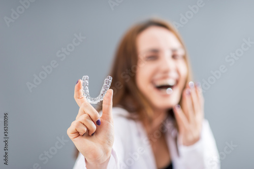 Beautiful smiling Turkish woman is holding an invisalign bracer in a studio with grey background