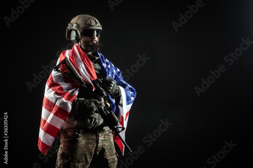 American soldier in military uniform with a gun holds the USA flag against a dark background, the elite troops of America, special forces