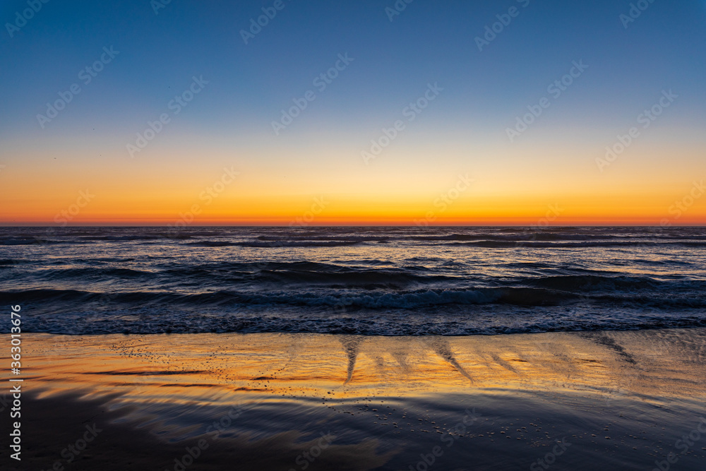 Orange sunset glows across the horizon and on wet sand on Cannon Beach in Oregon