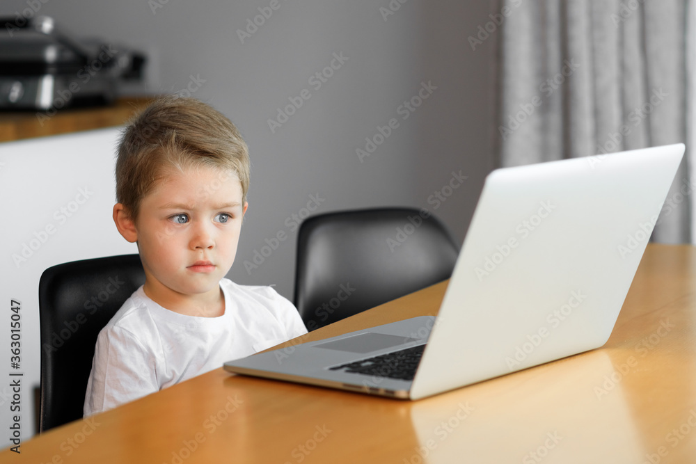 A young boy using a laptop computer sitting on top of a tableundefined at home A young boy using a laptop computer sitting on top of a tableundefined at home
